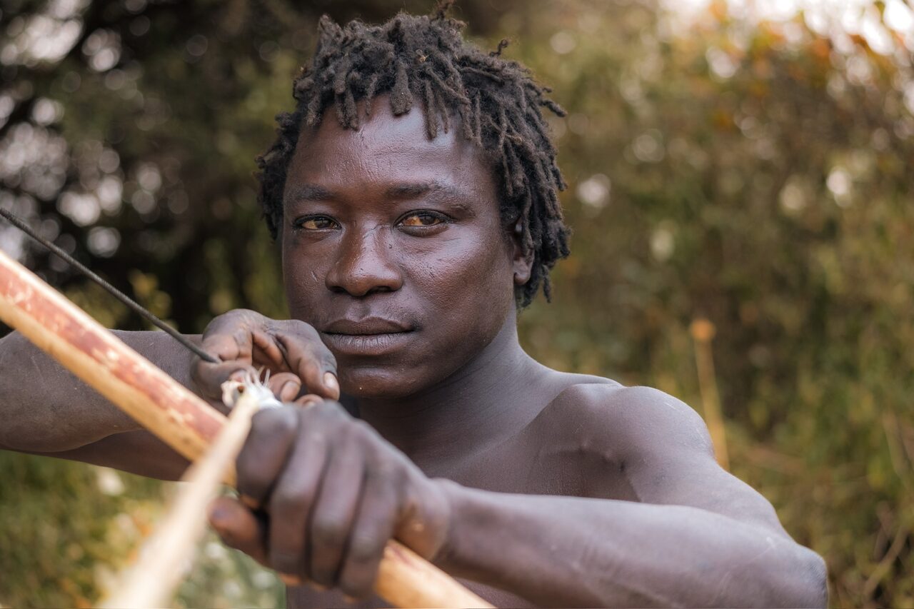 Young Hadzabe archer drawing back his bow, eyes fixed on the target